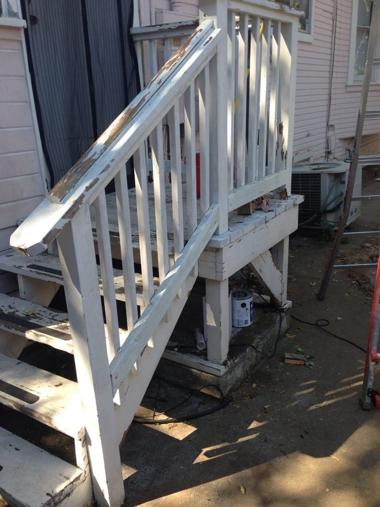 Exterior wooden stairs and railing before work, with the old white paint flaking away in sheets and the handrail, posts and stair treads weathered back to bare grey wood.