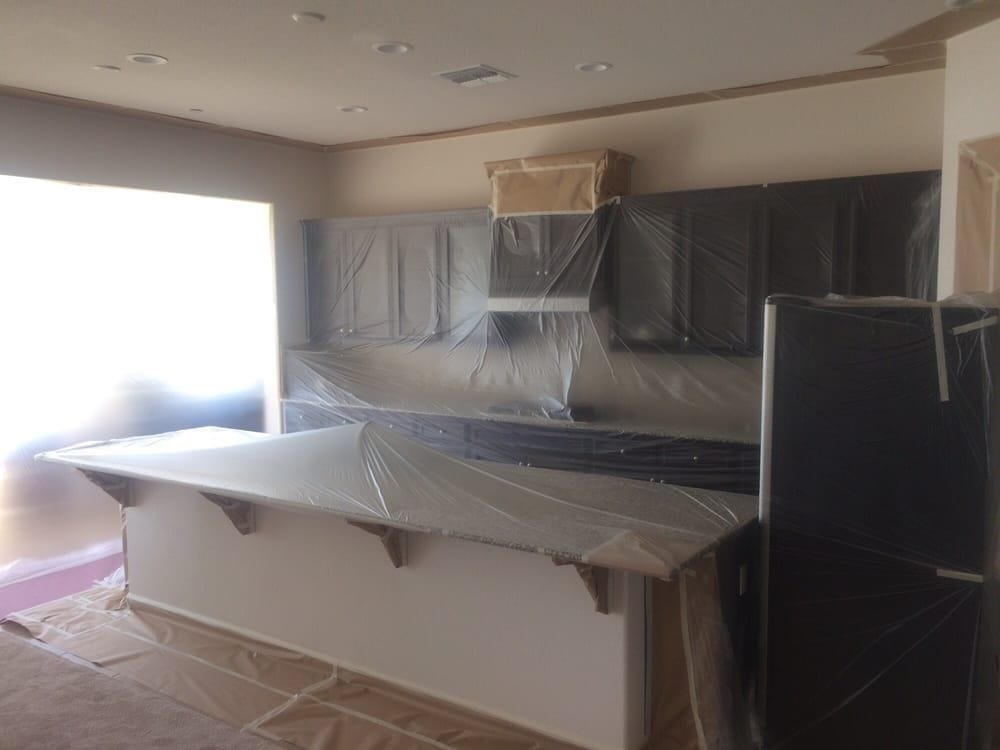 A Folsom kitchen masked before spraying. Plastic is taped over every cabinet door and the range hood, the island and countertops are sheeted, and paper covers the floor, leaving only the walls and ceiling exposed.
