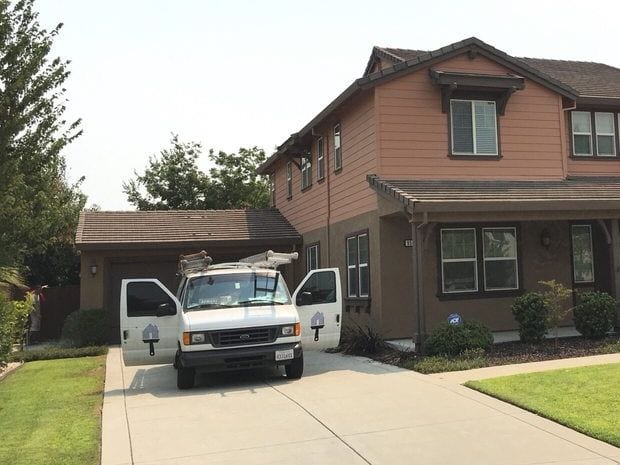 A two-storey house with freshly painted siding, trim and fascia, and the painting van parked on the driveway with its cab doors open and ladders on the roof rack.